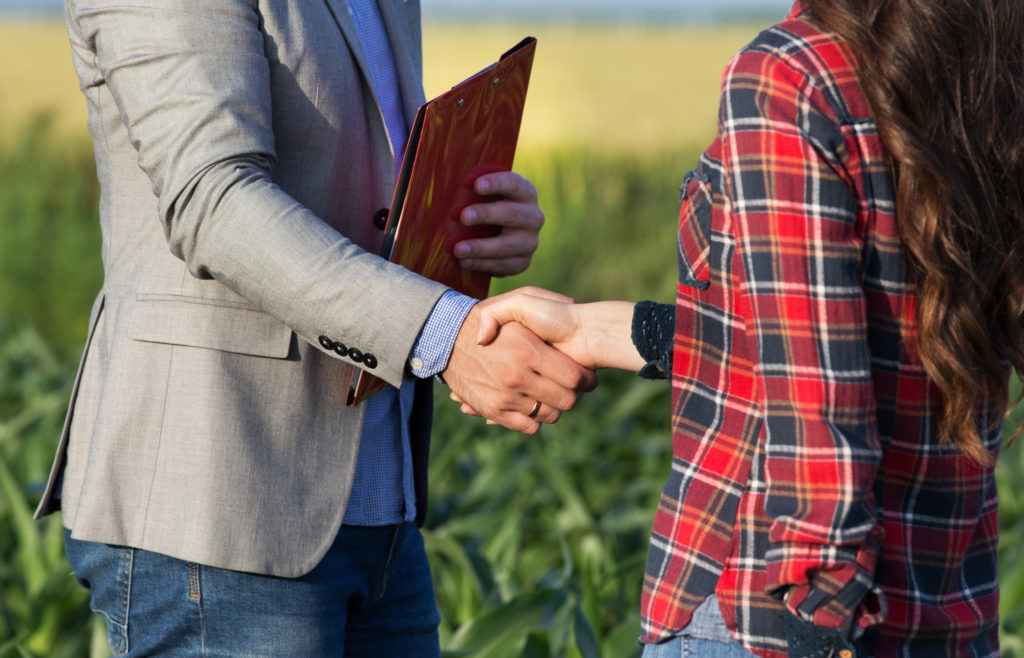 Farmer woman and businessman shaking hands in field